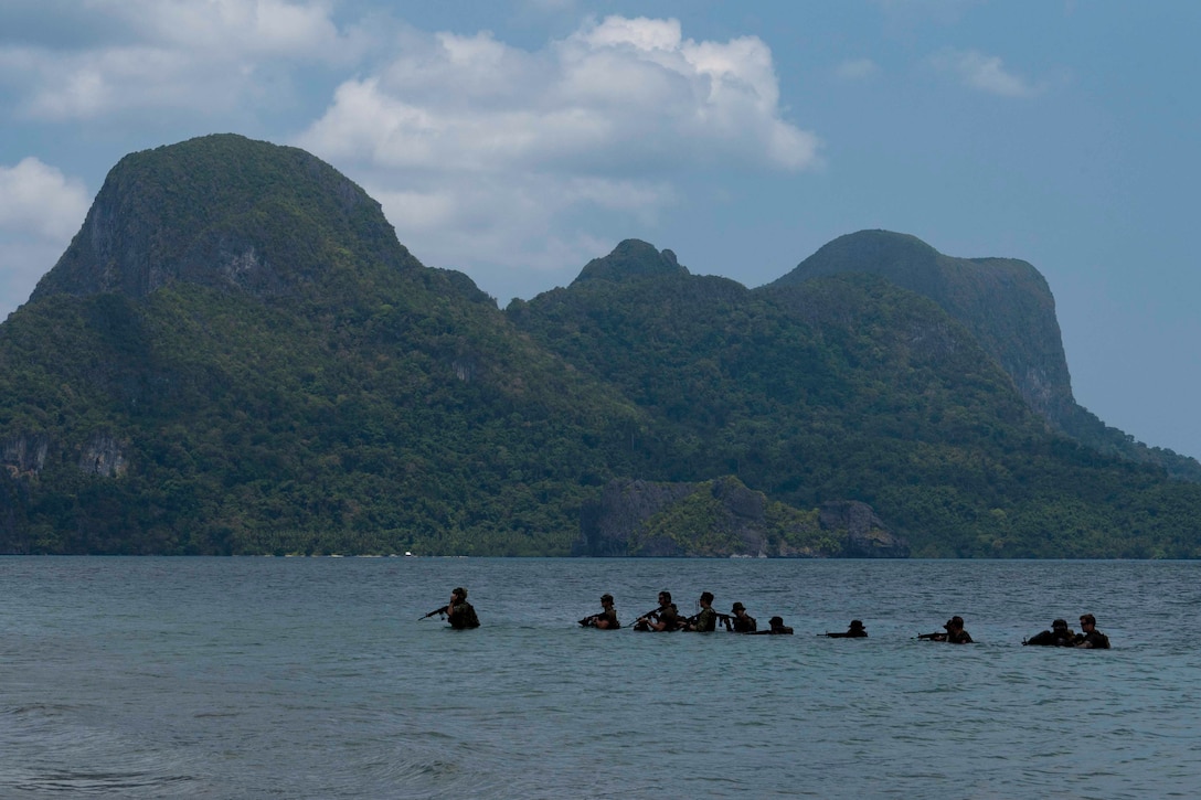 Sailors move through a body of water in a line with a mountain in the background.