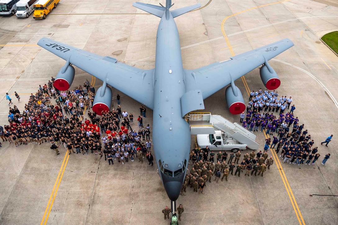 An overhead look at airmen and others standing around a parked aircraft.