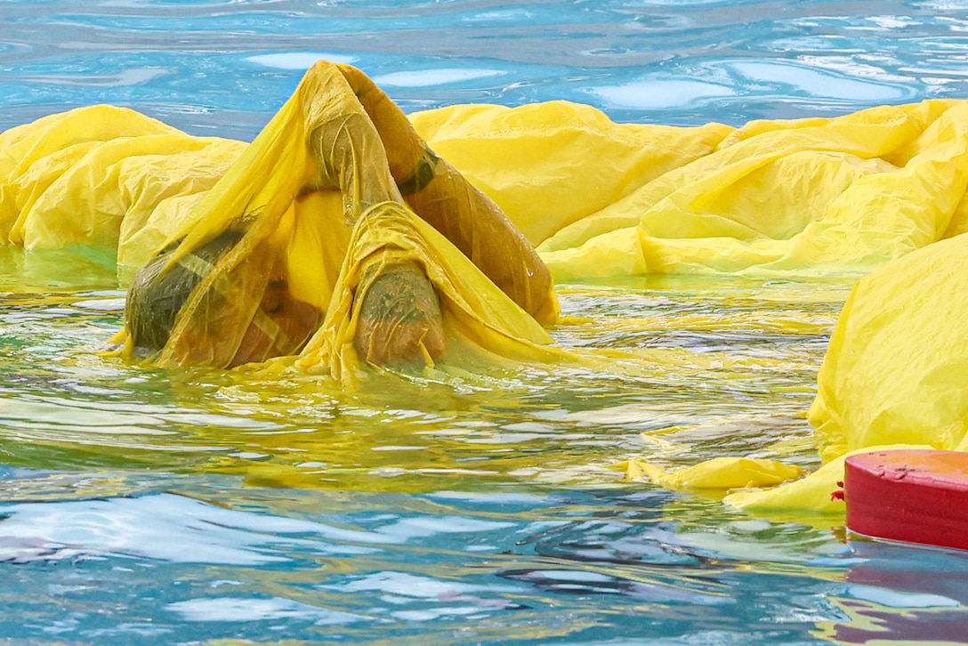 A Marine swims in a pool under a yellow parachute.