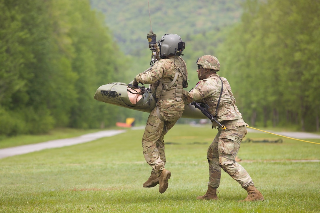 A soldier assists a fellow soldier and dummy on stretcher attached a hoist.