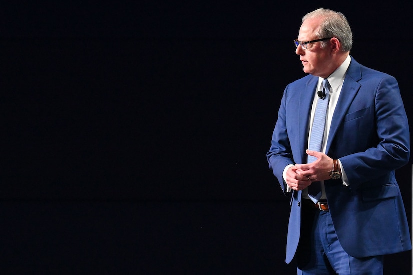 A man in a suit speaks on a stage.