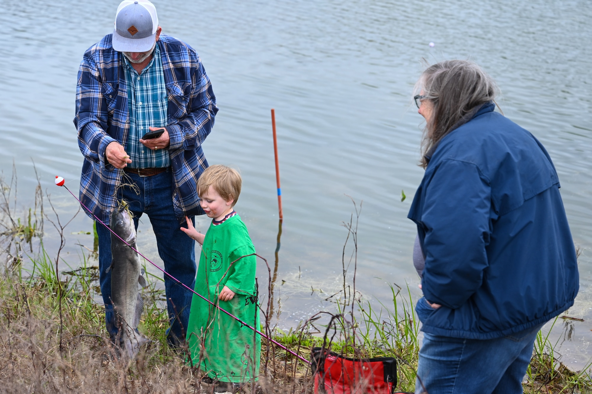 A child catches a fish with his grandparents at the 97th Civil Engineer Squadron environmental flight’s annual fishing derby at Altus Air Force Base, Oklahoma, April 28, 2023. The fishing derby encouraged Airmen and families to connect with nature and wildlife on base. (U.S. Air Force photo by Airman 1st Class Heidi Bucins)