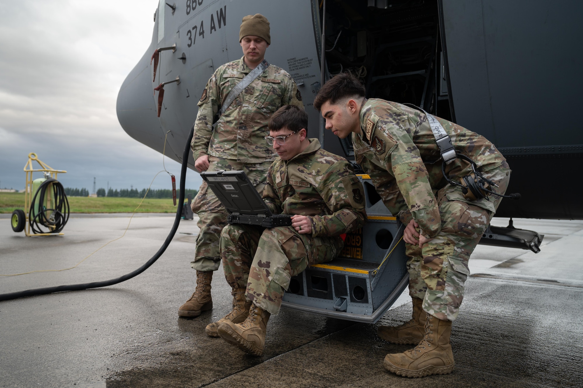 Three men look at a computer outside on a flightline by a plane.
