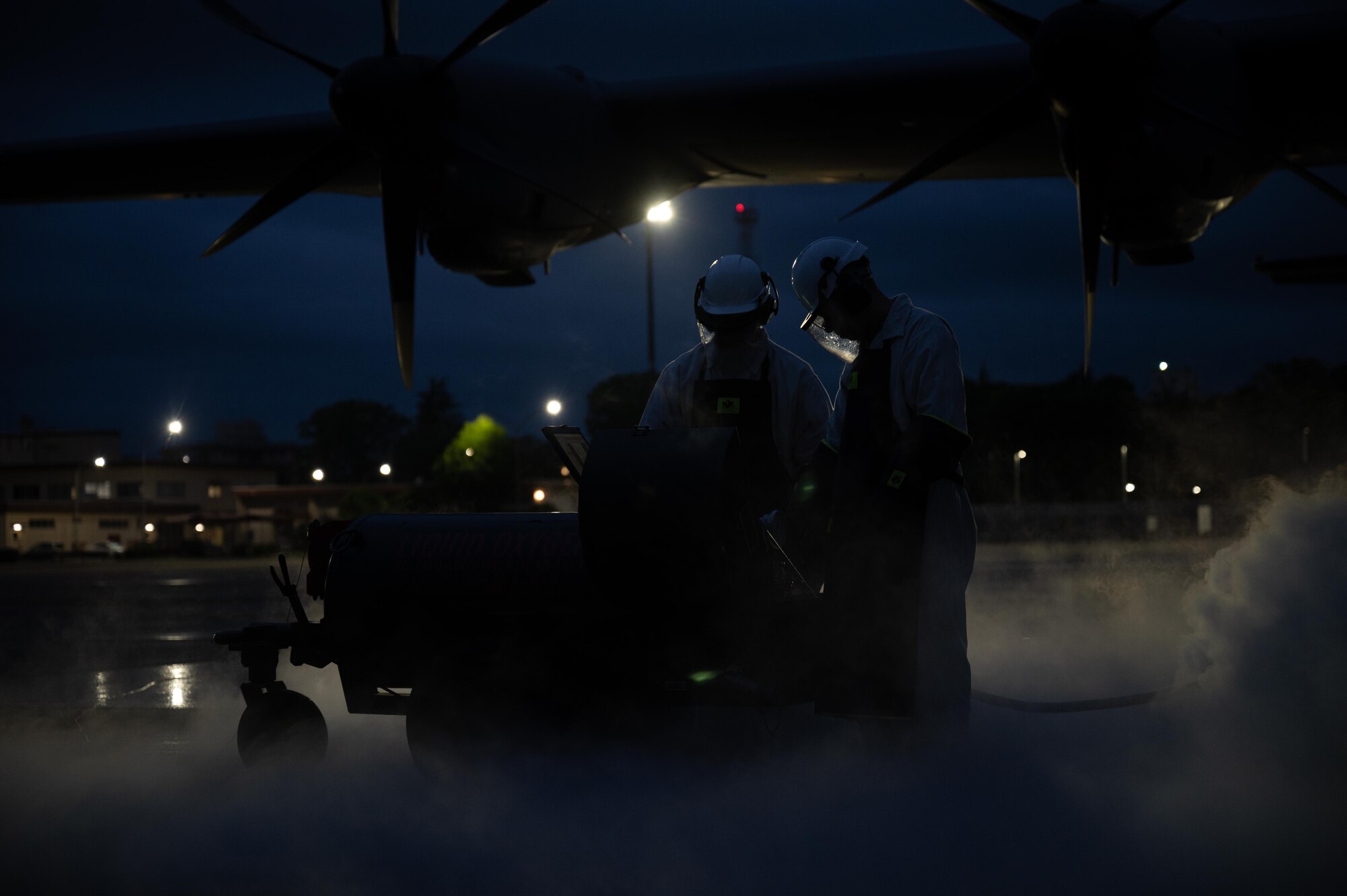 Two men refill a plane at night.