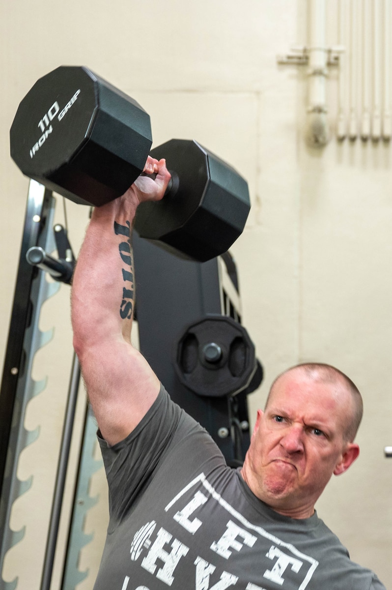Master Sgt. Ryan Kelly, a 934th Maintenance Squadron flight chief, overhead presses a dumbbell for a strongman competition at the fitness center on Minneapolis-St. Paul Air Reserve Station, Minneapolis, on April 20, 2023. This is the first strongman competition held by the 934AW. (U.S. Air Force photo Chris Farley)