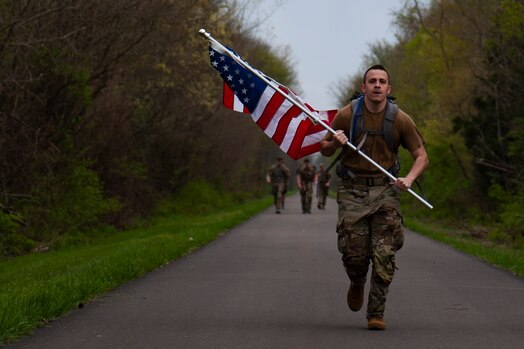  U.S. Air Force Senior Airman Abraham M. Coss, a member of the Signals Analysis Squadron, National Air and Space Intelligence Center, carries the U.S. flag while participating in the Bataan Memorial Death March in Beavercreek, Ohio, April 14, 2023. Airmen and Guardians from NASIC participated in this event to commemorate the combined 10,000 American and Filipino soldiers who died in the Philippines during the Bataan Death March in April 1942.