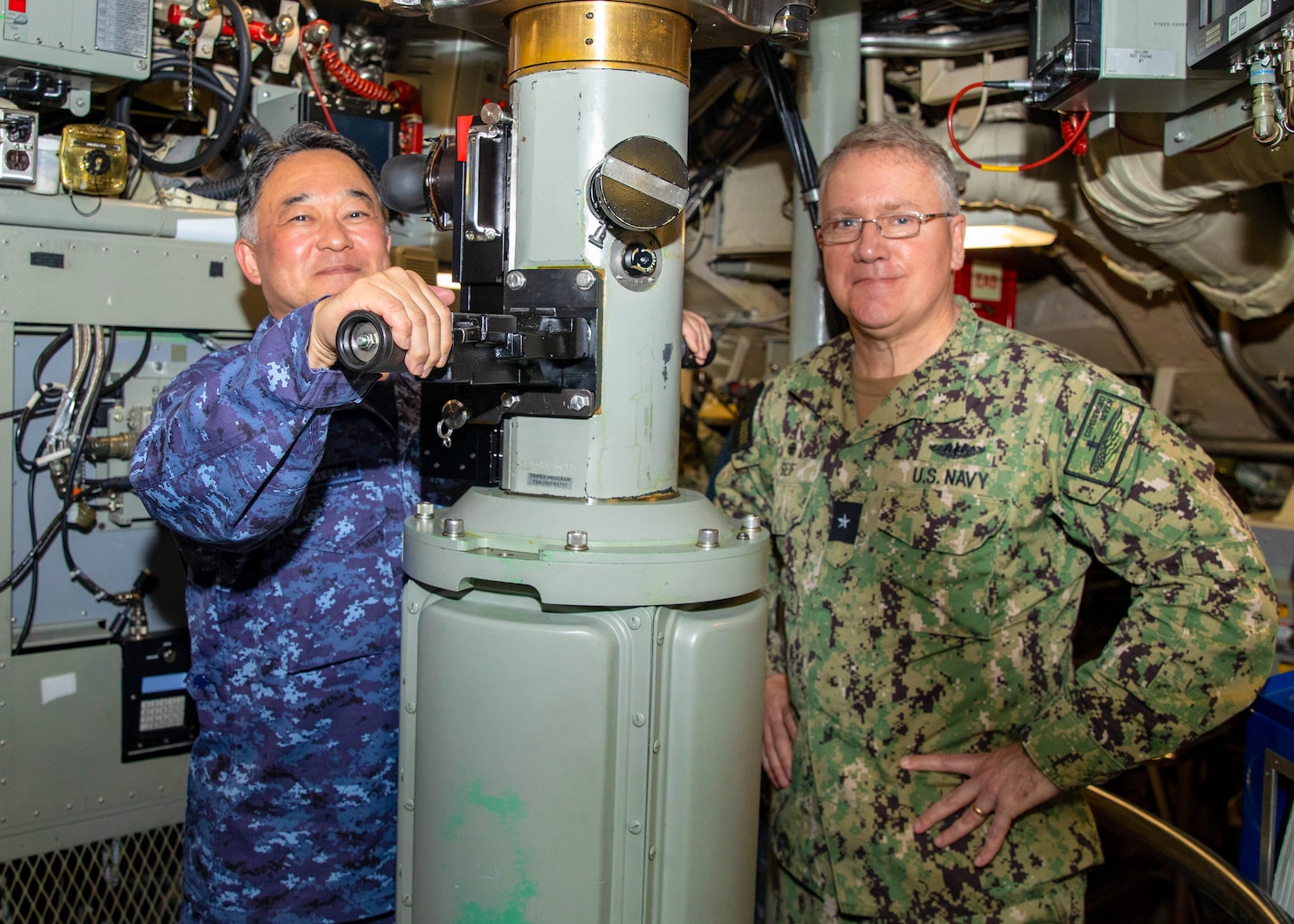 Japan Maritime Self-Defense Force Vice Adm. Tateki Tawara, commander, Fleet Submarine Force, left; poses for a photo with U.S. Navy Rear Adm. Rick Seif, commander, Submarine Group 7; while using the periscope aboard the Ohio-class ballistic missile submarine USS Maine (SSBN 741), April 18. During their time at sea aboard the submarine, the senior leaders were provided tours and demonstrations of the unit’s capabilities, which operates globally under U.S. Strategic Command.