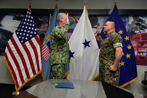 Navy officer with hand raised administered the oath of office to a Marine officer, with hand raised.