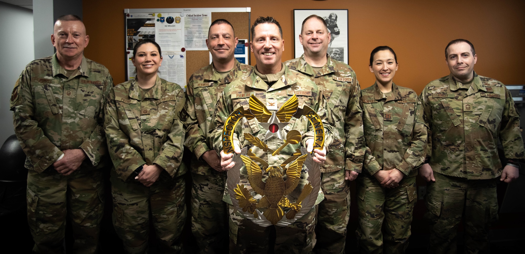 A group of seven Airmen stand in a row, holding a large metal badge in the center