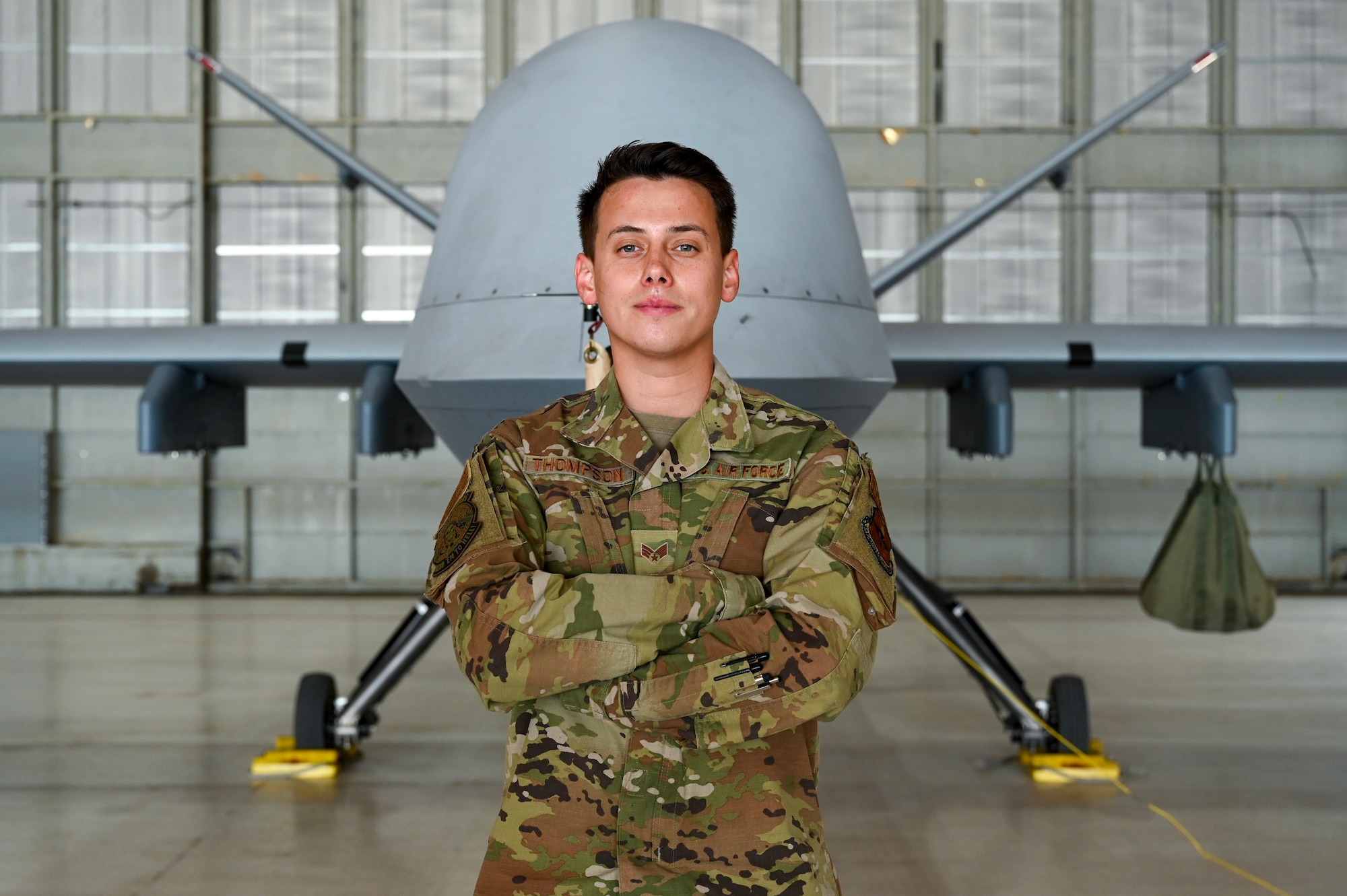 U.S. Air Force Senior Airman Alejandro Thompson, 29th Aircraft Maintenance Unit MQ-9 dedicated crew chief, poses in front of an MQ-9 at Holloman Air Force Base, New Mexico, May 3, 2023.