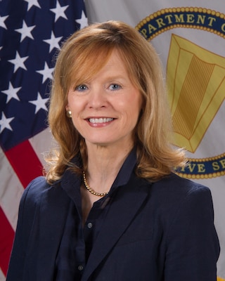 Photo of lady dressed in blue blazer and blue shirt in front of flag