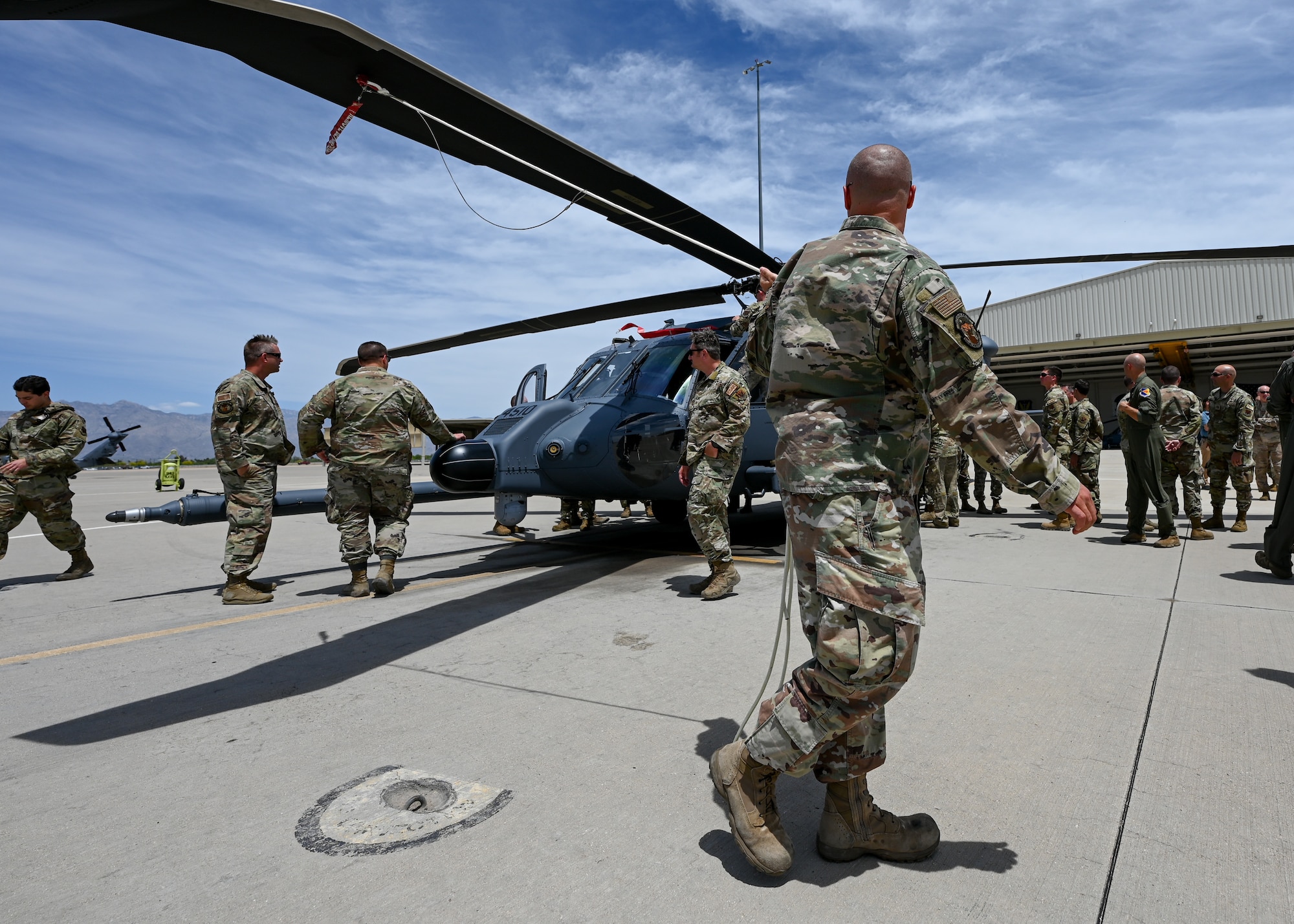 A man in a military uniform holds a rope attached to the rotor of a helicopter.