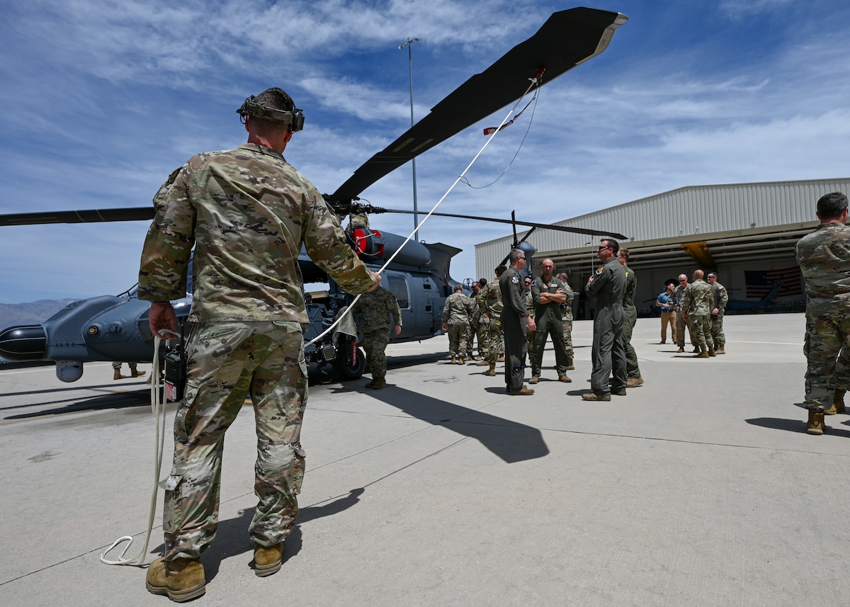 A man in a military uniform holds a rope attached to the rotor of a helicopter.