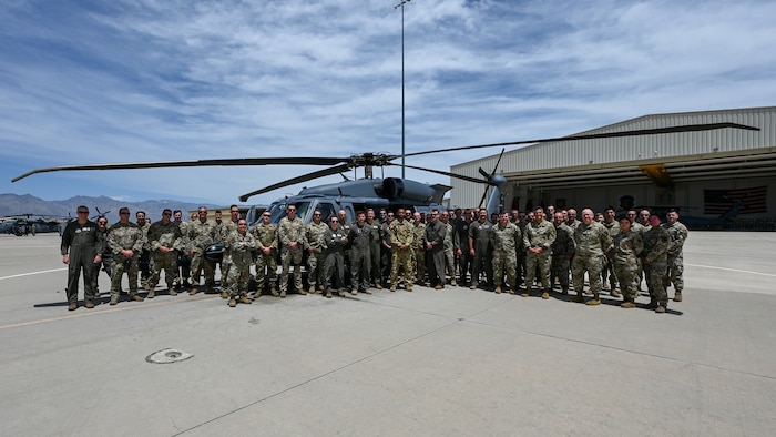 A group of people in military unforms pose for a group photo in front of a helicopter.