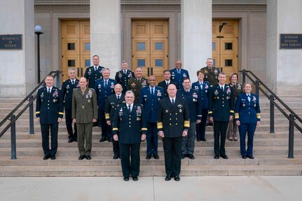 Multiple men and women in dress military uniform stand on steps and pose for a photo.