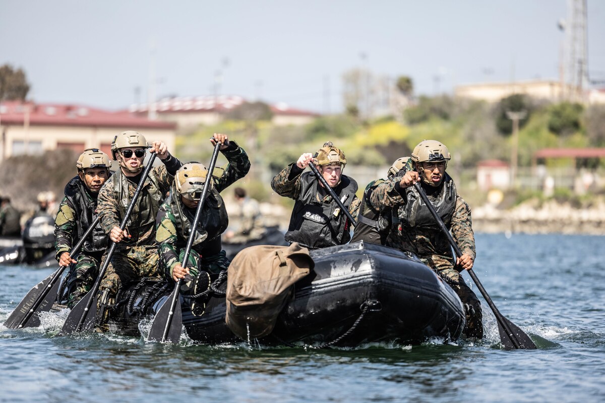 Marines paddle through a body of water in a small inflatable boat.