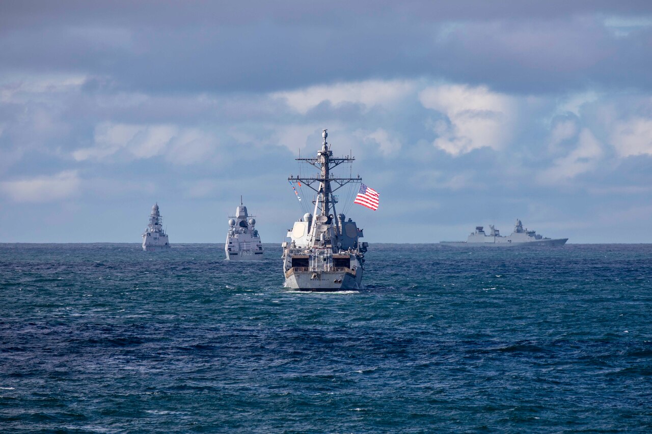 Multiple naval vessels move across the ocean.