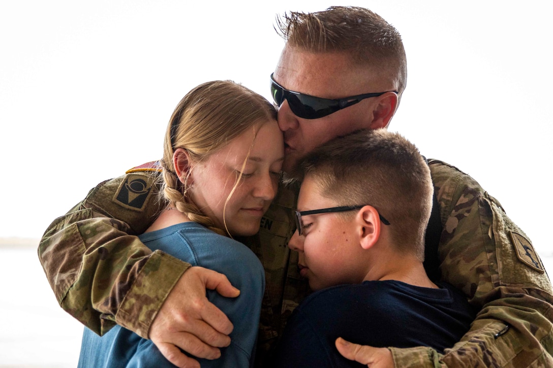 A soldier hugs two people.