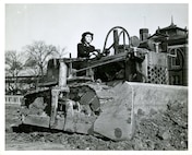 "GROUND BREAKING FOR NEW SPAR BARRACKS -- SPAR RITA KEITH, seaman second class, lends a hand on the bulldozer which is breaking ground for the new Washington, D.C. barracks for members of the Women's Reserve of the U.S. Coast Guard Reserve, across from the Smithsonian Institute.  She drives cars at Coast Guard Headquarters now, but she used to drive a delivery truck for a cleaning establishment in her hometown _____. Her husband, Rosel Keith, shipfitter 3rd class, USN, is in the South Pacific." USCG Photo Lab. # 3485.