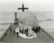 Coast Guardsmen are removing the restraining net from the balloon prior to sending it aloft. The fins are not yet inflated, as they will automatically fill with air as the balloon rises, through a wind tunnel which runs the length of the balloon from the nose to the fins. This photo series was made on March 7-8, 1952, during a test cruise of the USCGC COURIER (WAGR-410),