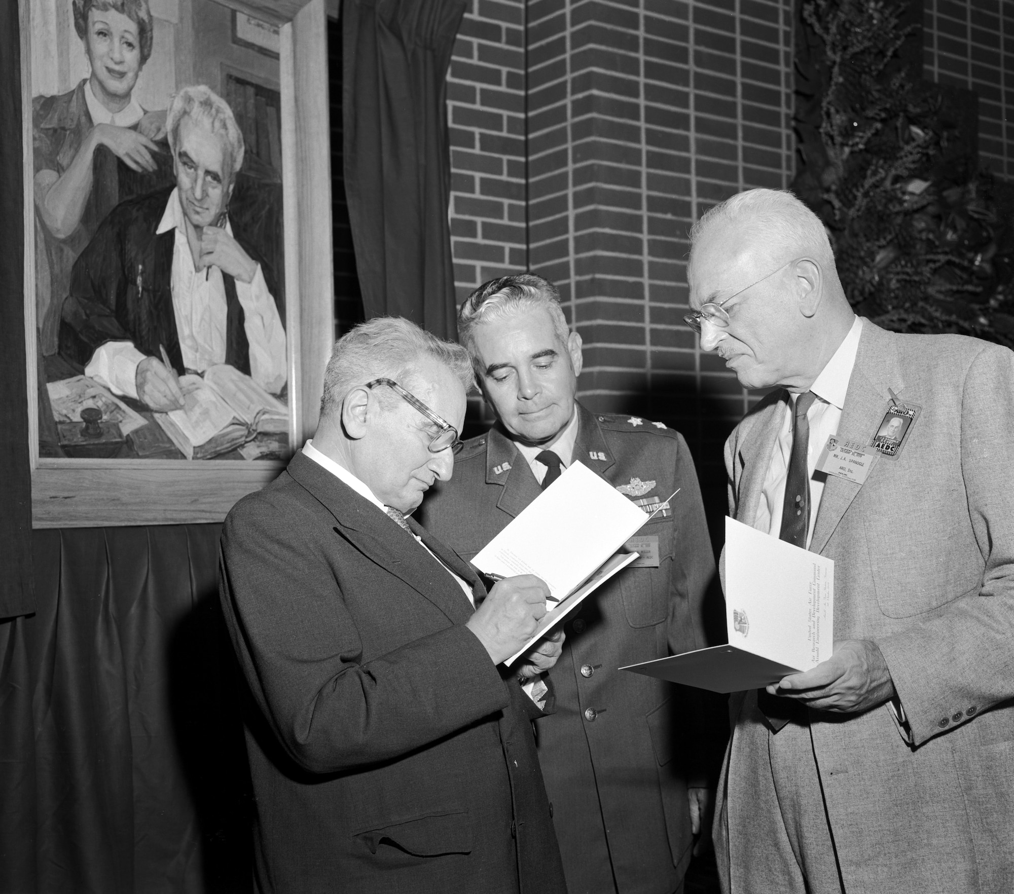 Dr. Theodore von Kármán, left, provides his autograph during a luncheon Oct. 30, 1959, at Arnold Air Force Base, Tenn., while revealing the portrait behind him of him and his sister Dr. Joesphine de Kármán. Also pictured is then-Maj. Gen. Troup Miller Jr., then-commander of Arnold Engineering Development Center, and J.A. Spanogle with the Arnold Research Organization. (U.S. Air Force photo)