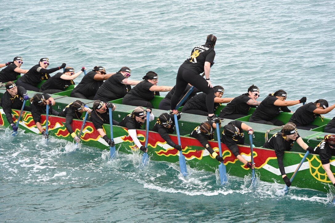 A coach talks to team members using oars to row in a dragon boat at sea.