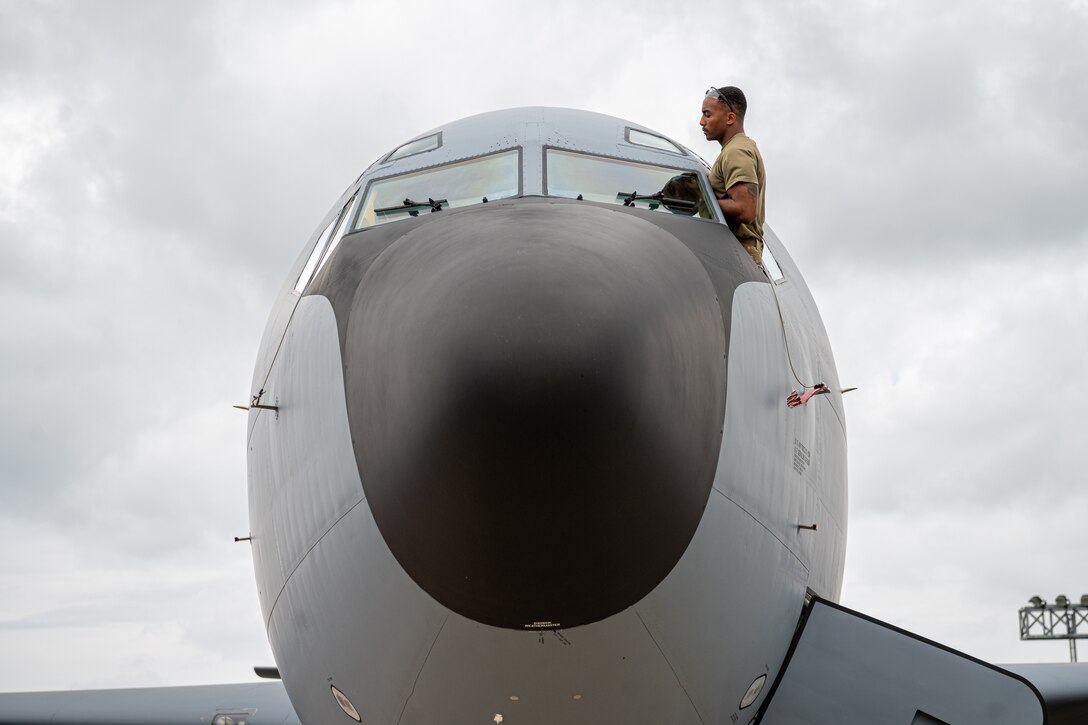 Ab airman sits in a window opening of a large aircraft and inspects another window.