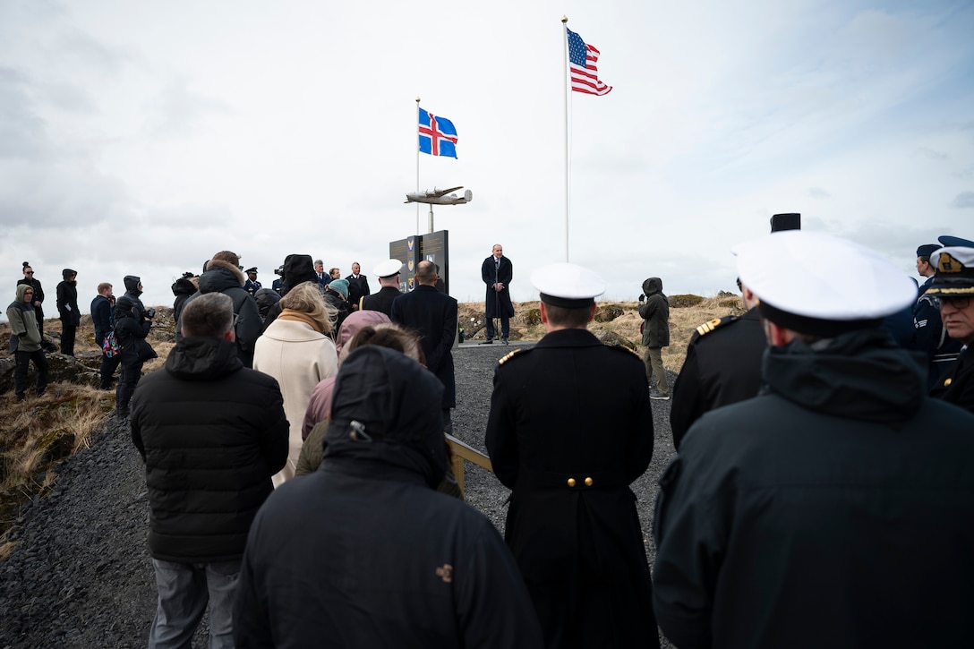 A man speaks to a crowd next to a monument.