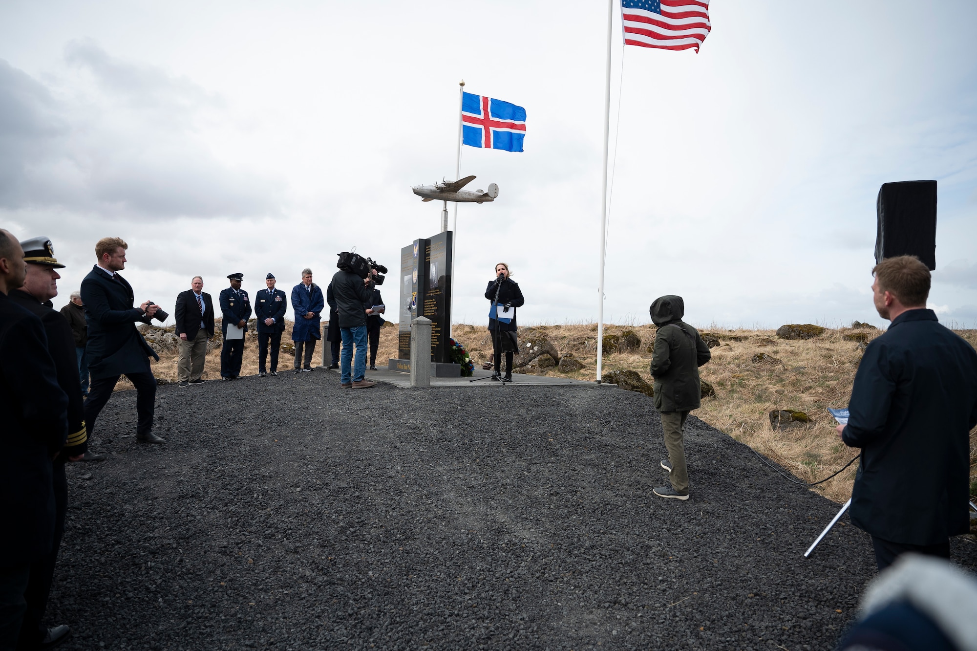 A woman speaks to a crowd next to a monument.