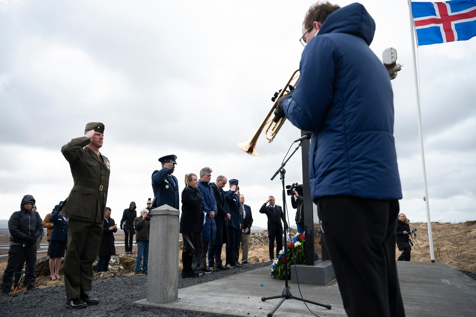 People in uniform salute while a man plays a trumpet.