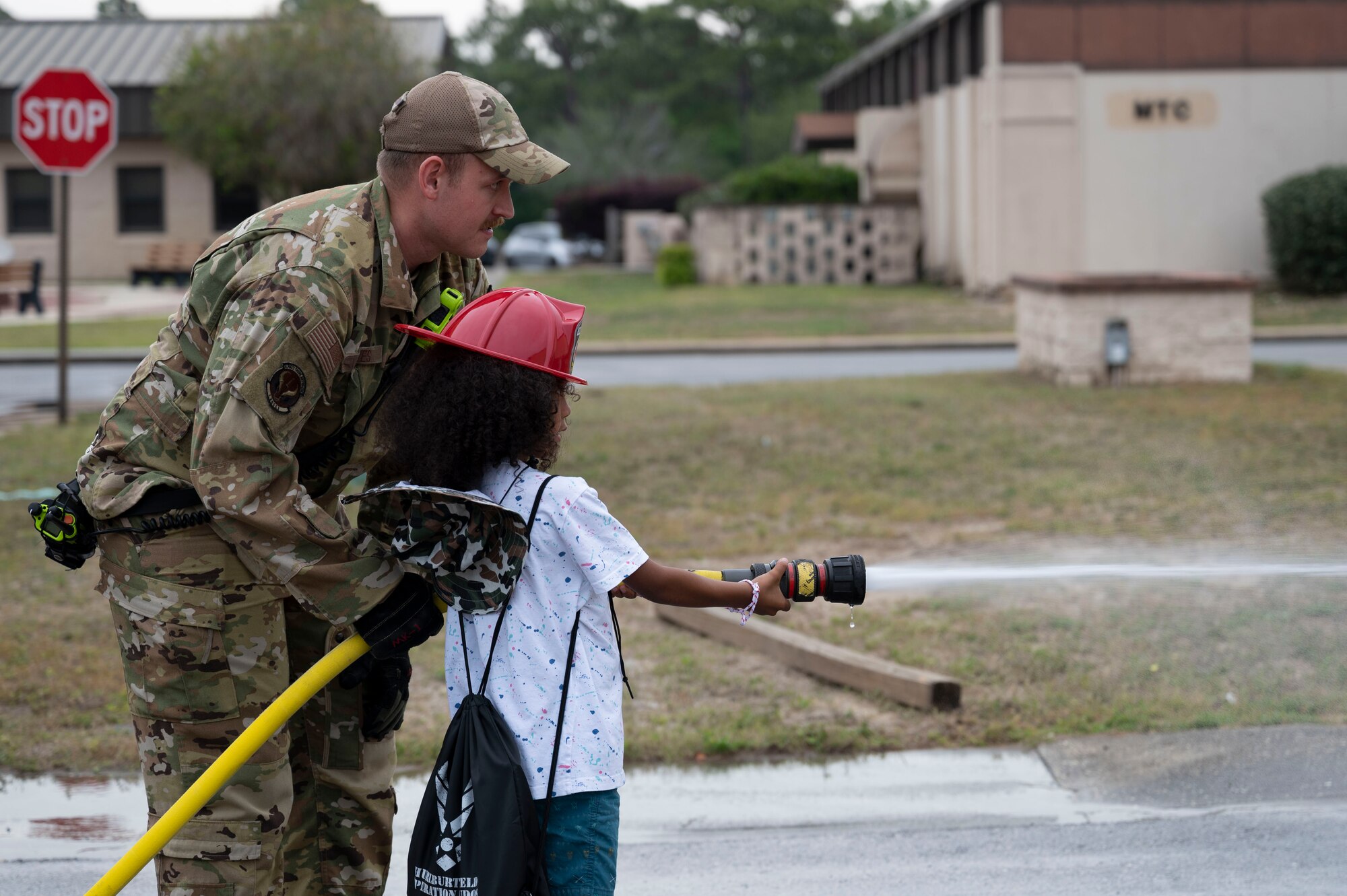 Senior Airman Preston Eaves, a 1st Special Operations Civil Engineer Squadron firefighter, helps a military child use a firehose during Operation Kids Understanding Deployment Operations at Hurlburt Field, Fla., April 29, 2023.