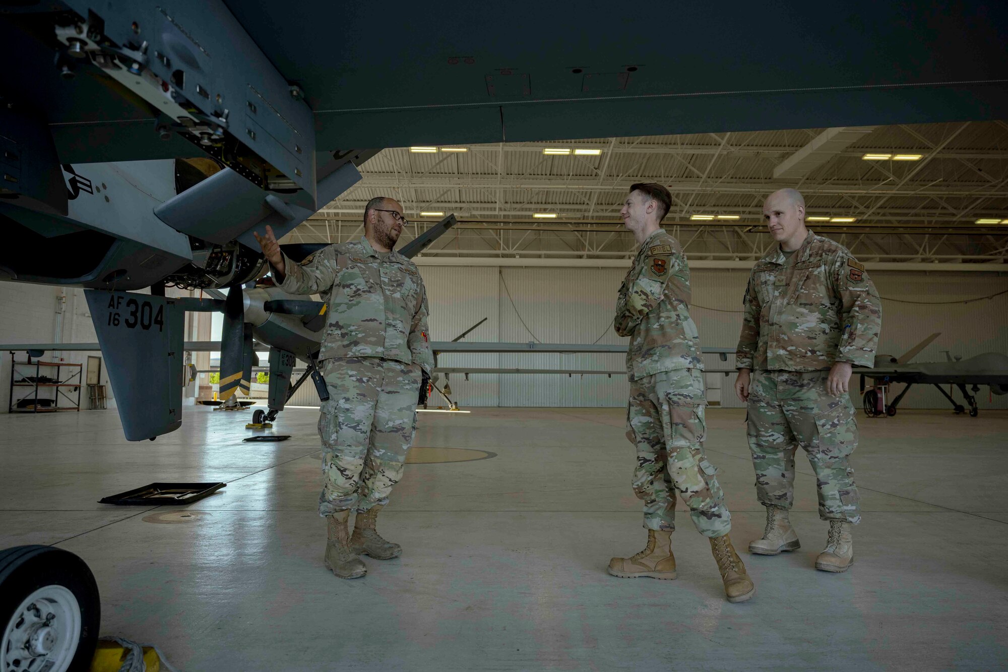 U.S. Air Force Staff Sgt. Keith Hundley, 9th Aircraft Maintenance Unit dedicated crew chief, left, gives a quick overview of the MQ-9 Reaper to two Airmen participating in a job swap event at Holloman Air Force Base, New Mexico, April 28, 2023. Three Airmen, from varying squadrons, spent the day with maintainers to learn the daily operations and procedures the 9th AMU conducts. (U.S. Air Force photo by Senior Airman Antonio Salfran)