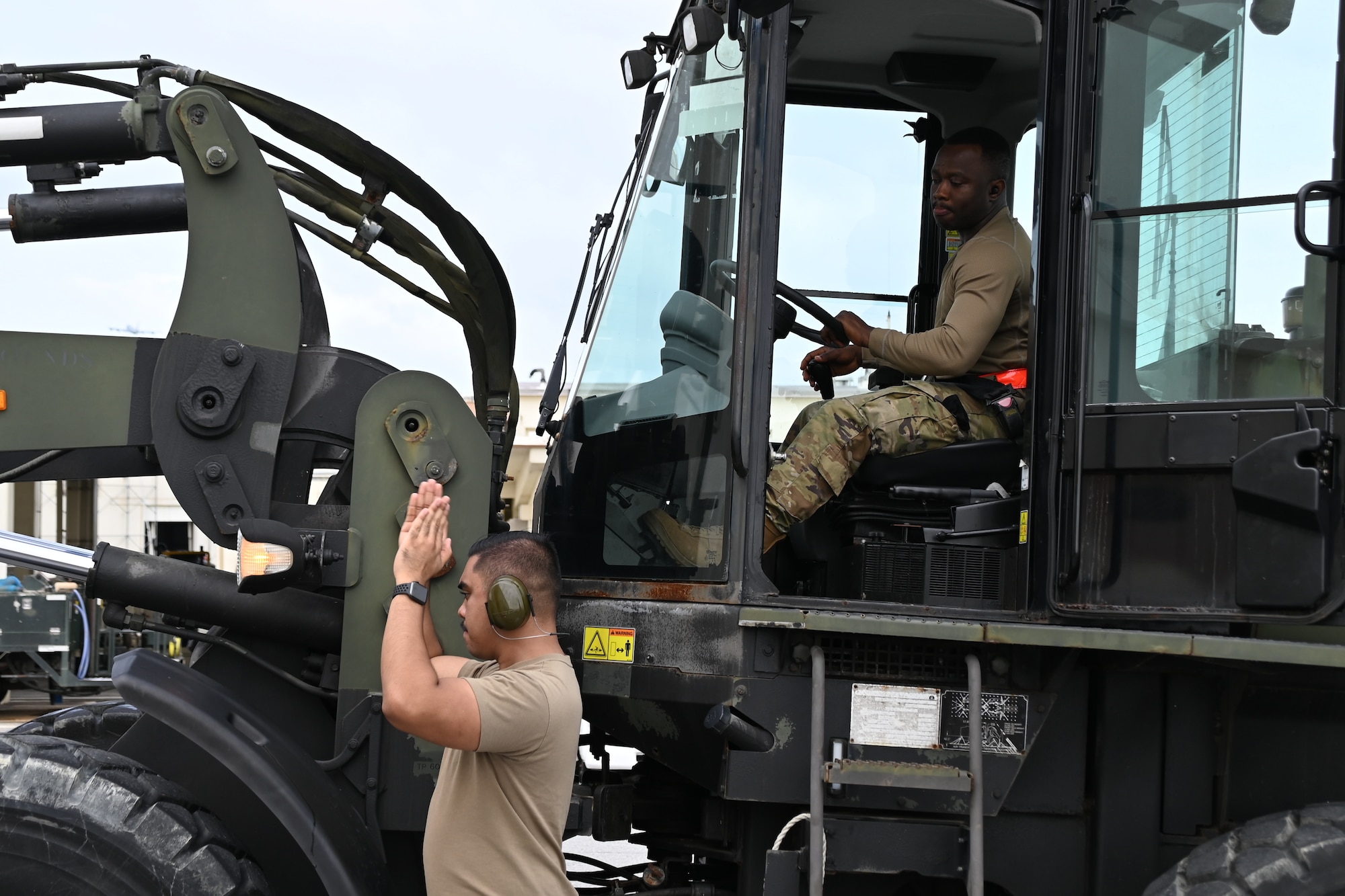 An airman gives ground guidance with his hands up to the driver of a forklift.