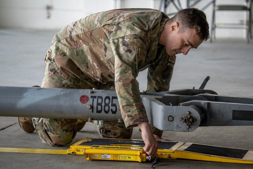 U.S. Air Force Tech. Sgt. Tyler Bowers adjusts the side of a mechanical pad that one of the wheels of an F-22 Raptor fighter jet will roll on to