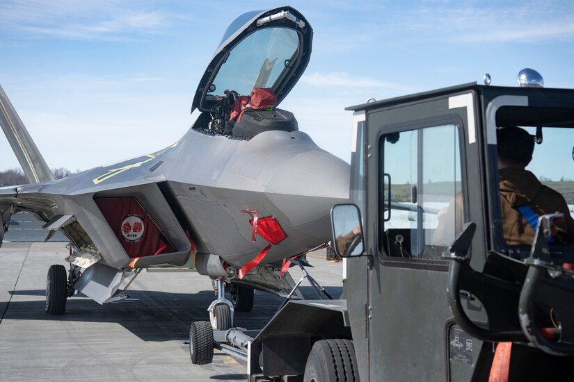 A towing vehicle pushes an F-22 into a position on a flighline