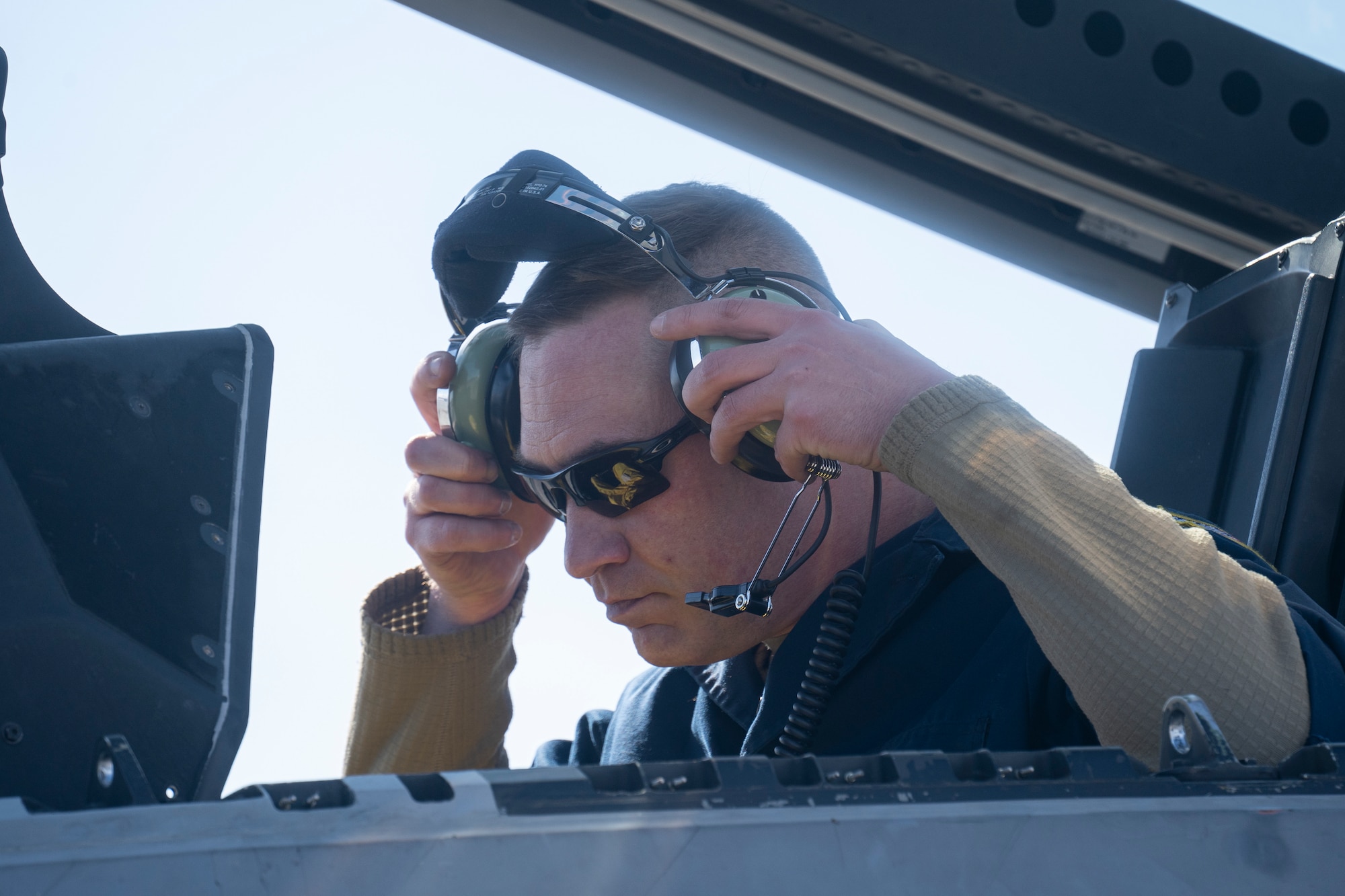 U.S. Air Force Master Sgt. Joshua Eller puts his headset on while in the cockpit of an F-22 Raptor fighter jet