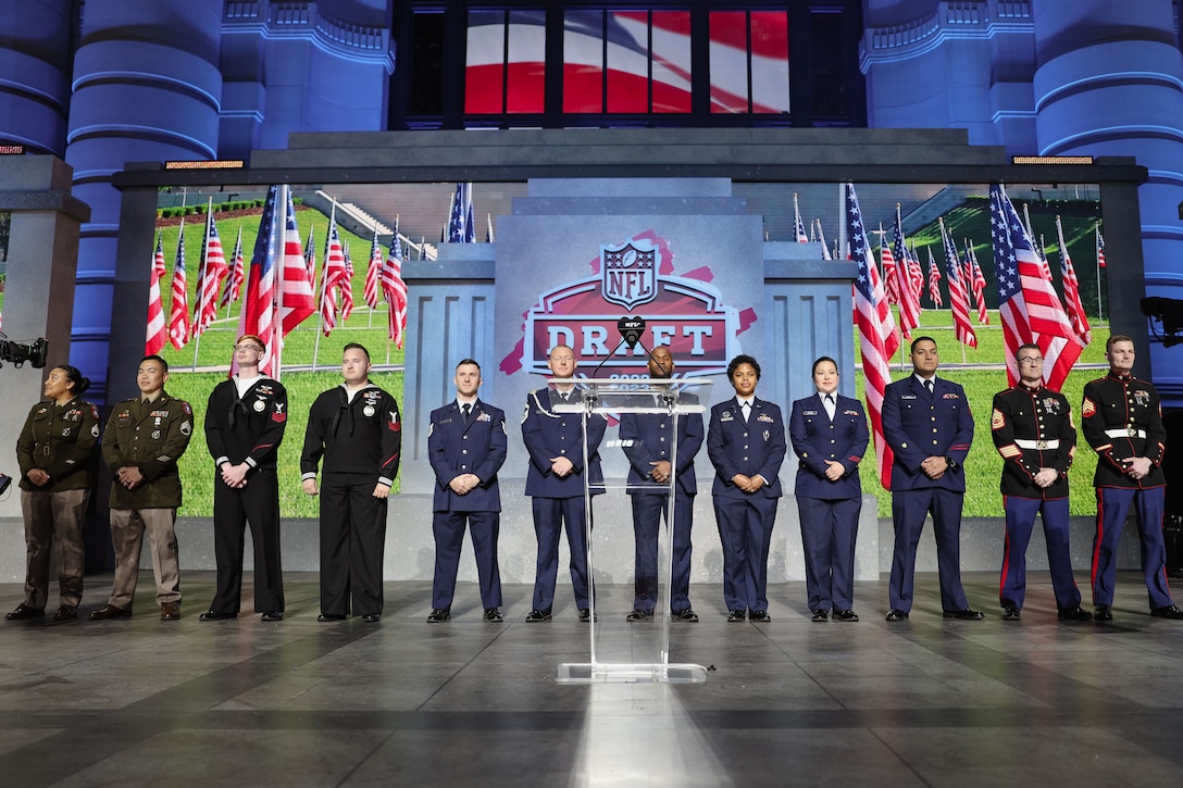 A group of service members in formal uniforms stand next to each other on a stage.