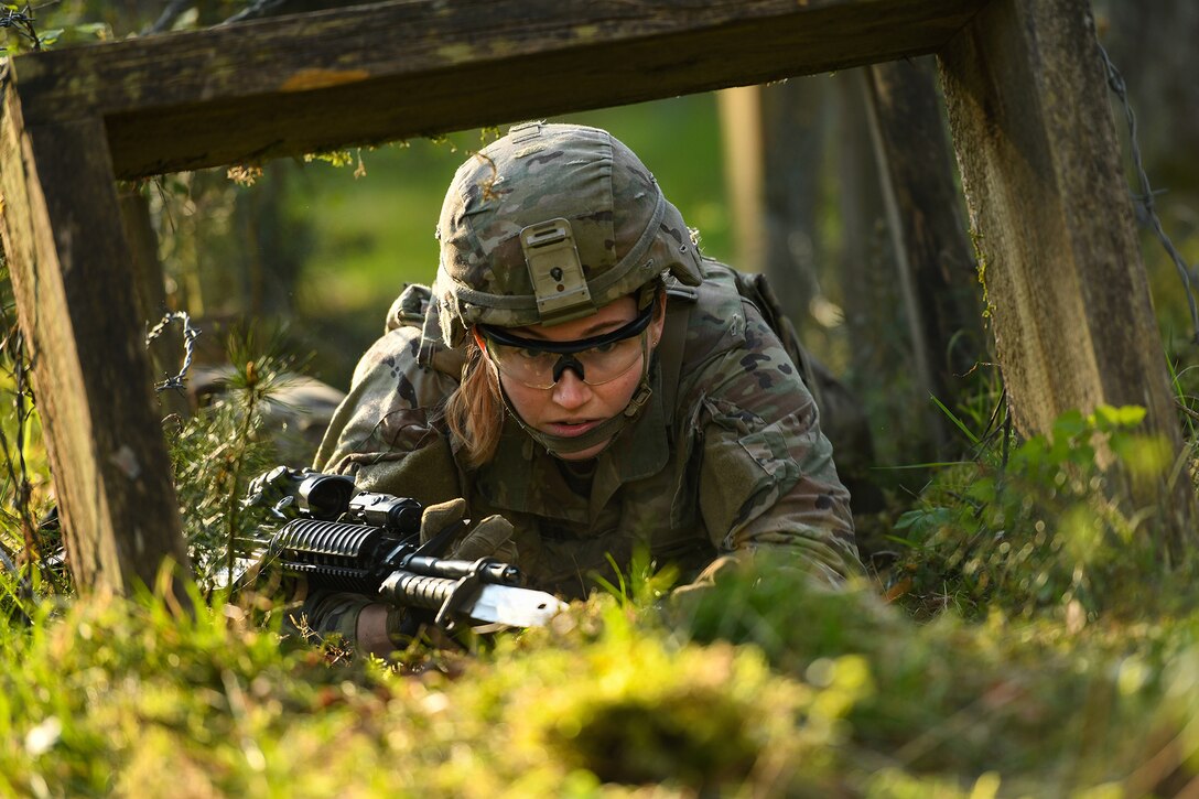 A soldier low-crawls in a grassy area.