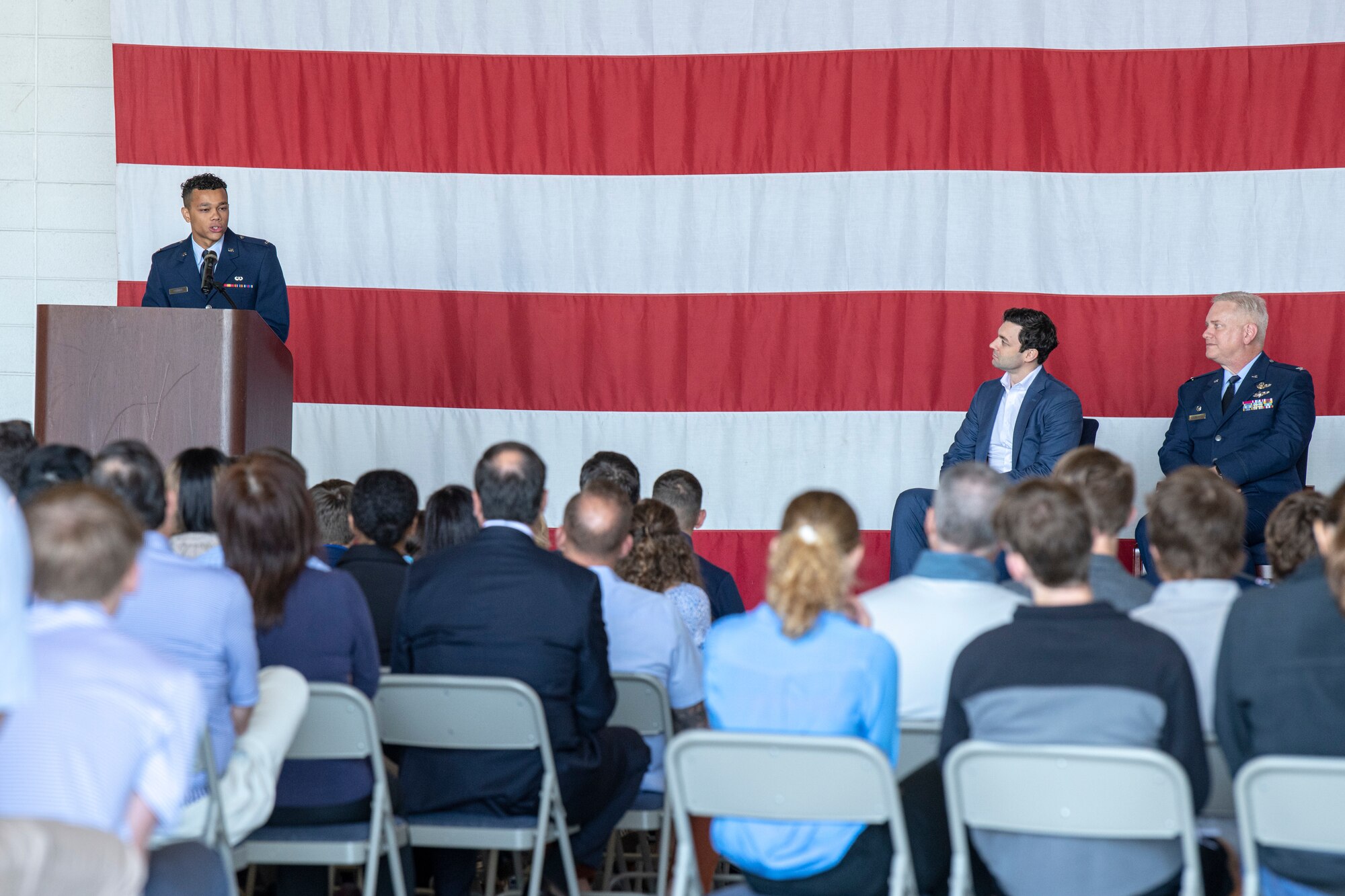a man in a blue military suit speaks to a crowd of students and parents