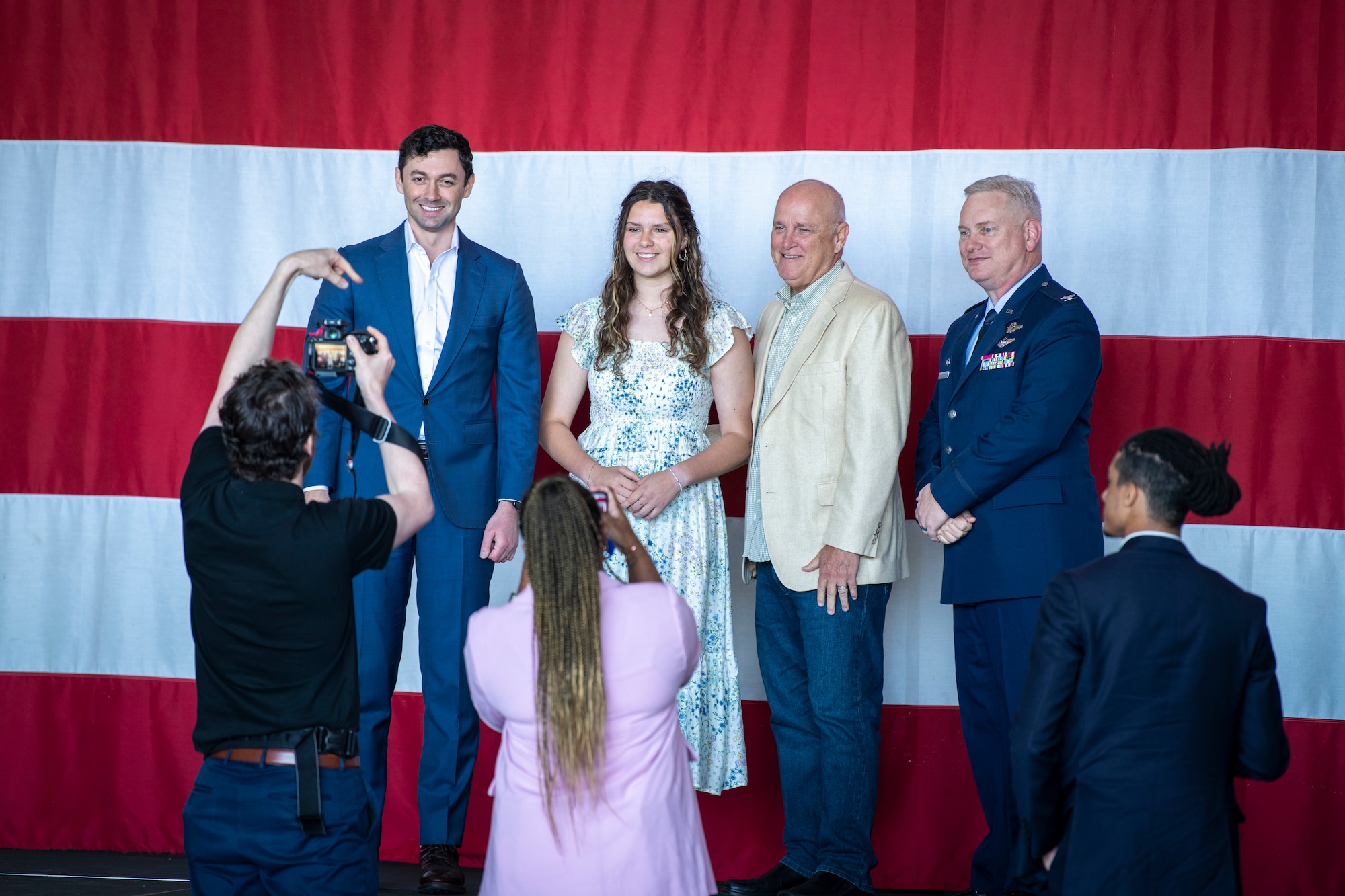 four people pose for a photo in front of a large American flag backdrop