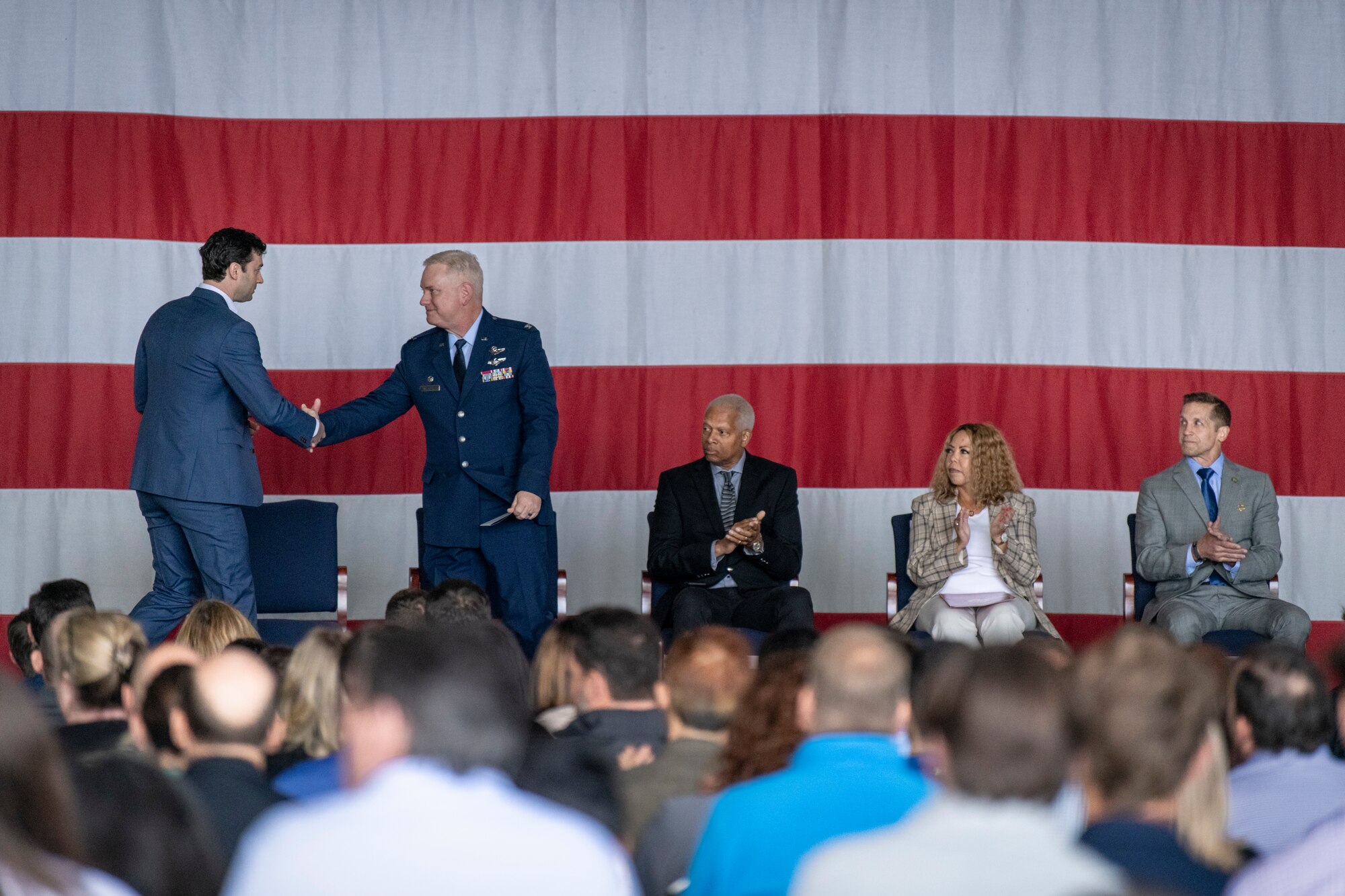 two men in blue suits shake hands while standing on a stage in front of a crowd of people