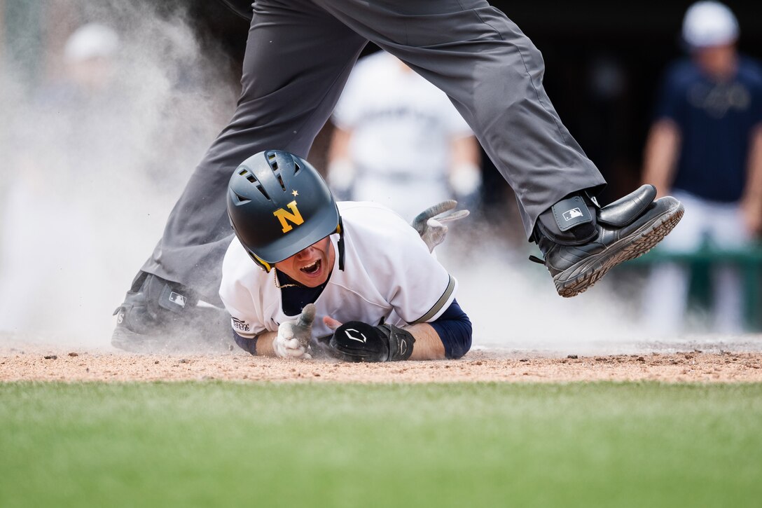A U.S. Naval Academy midshipman slides under an umpire’s legs during a baseball game.