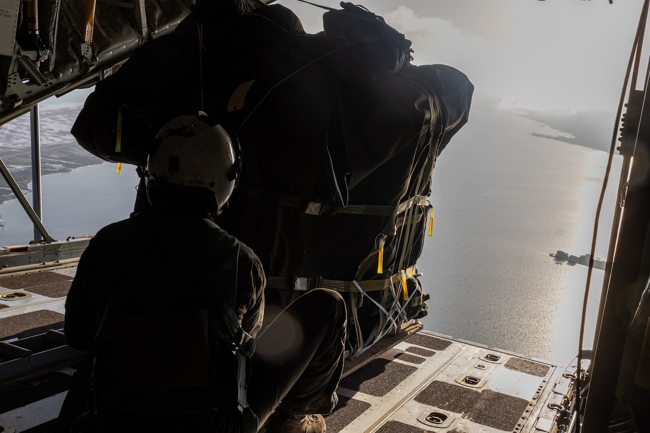 A Marine pushes cargo out of an airborne aircraft.