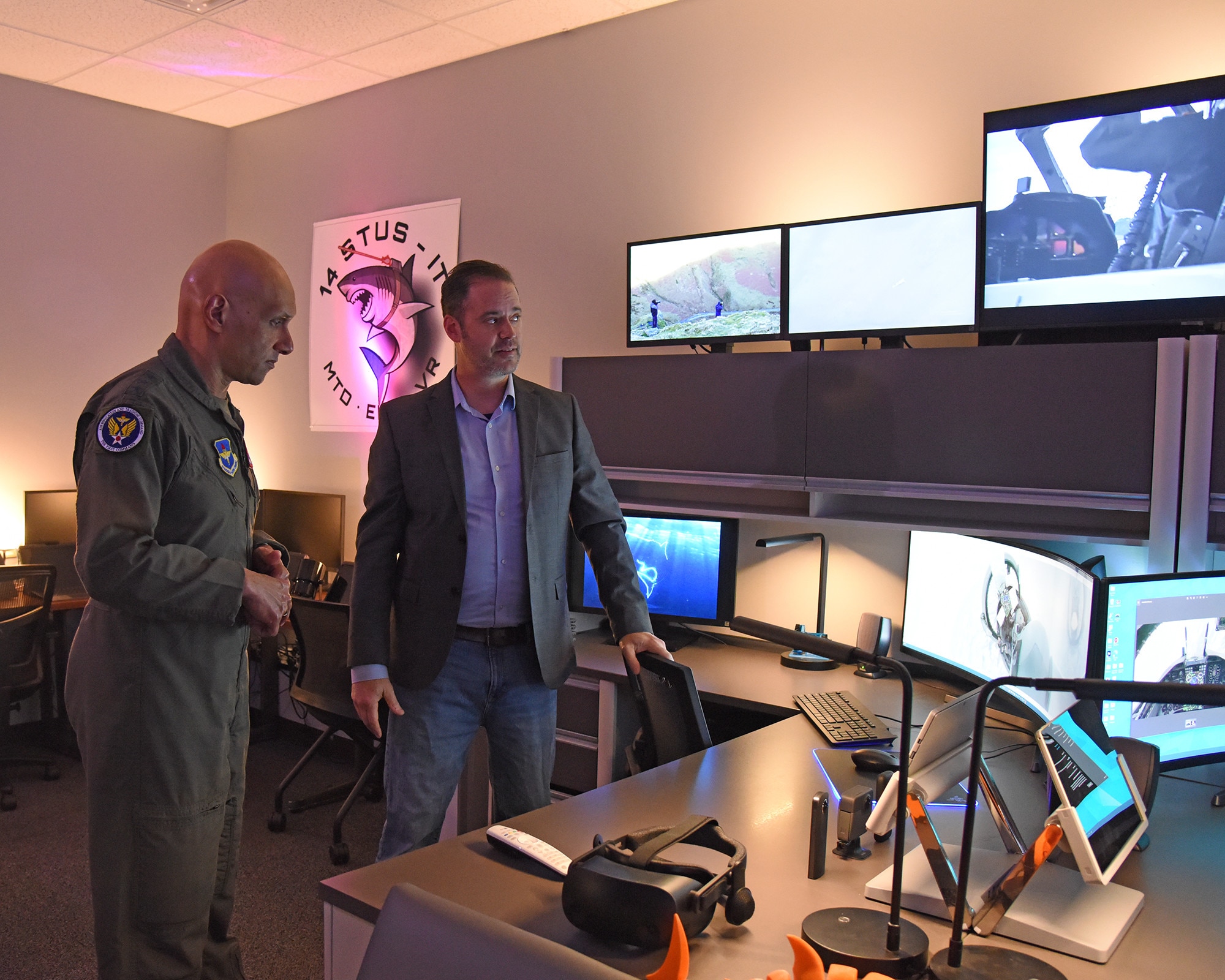 Lt. Gen. Brian Robinson and Mr. Aaron Lorenz stand in front of several computers in the Task Force 14 building.