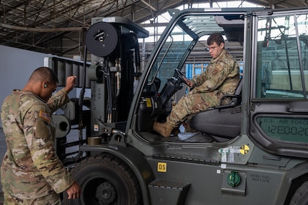 A service member helps guide a forklift onto a scale.