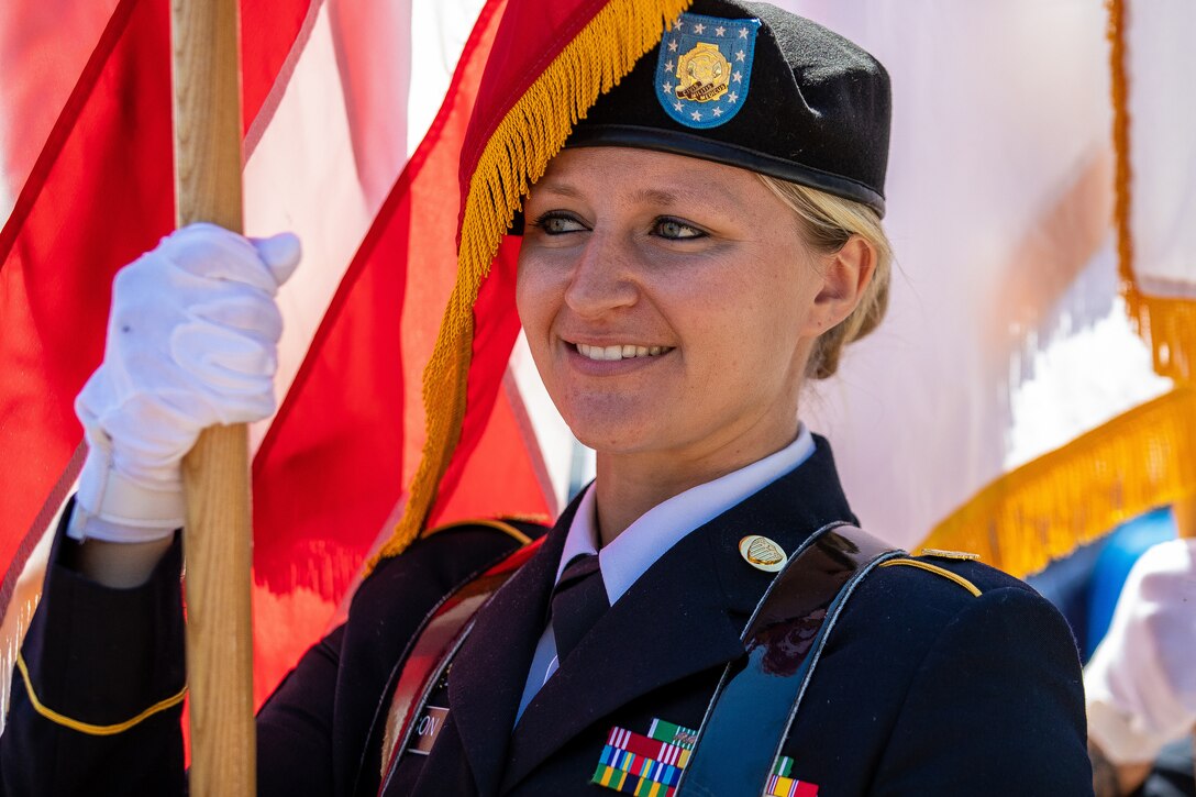 A soldier smiles as she holds the staff of a flag.