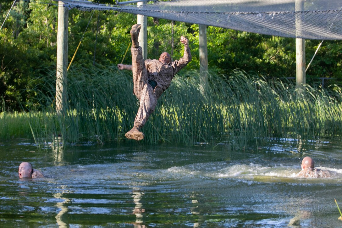 A Marine recruit prepares to land in the water as two others swim below him.