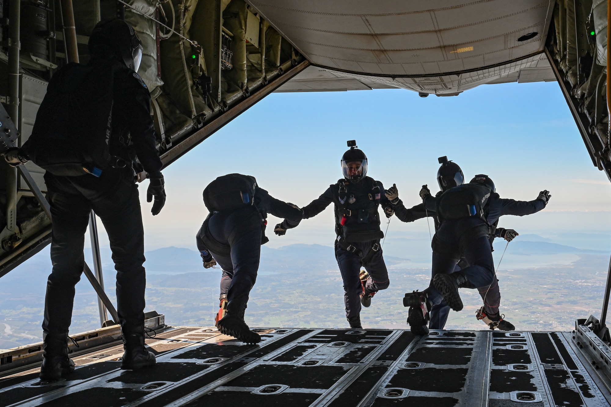 Airmen parachute jump out of the back of a C-130J Super Hercules