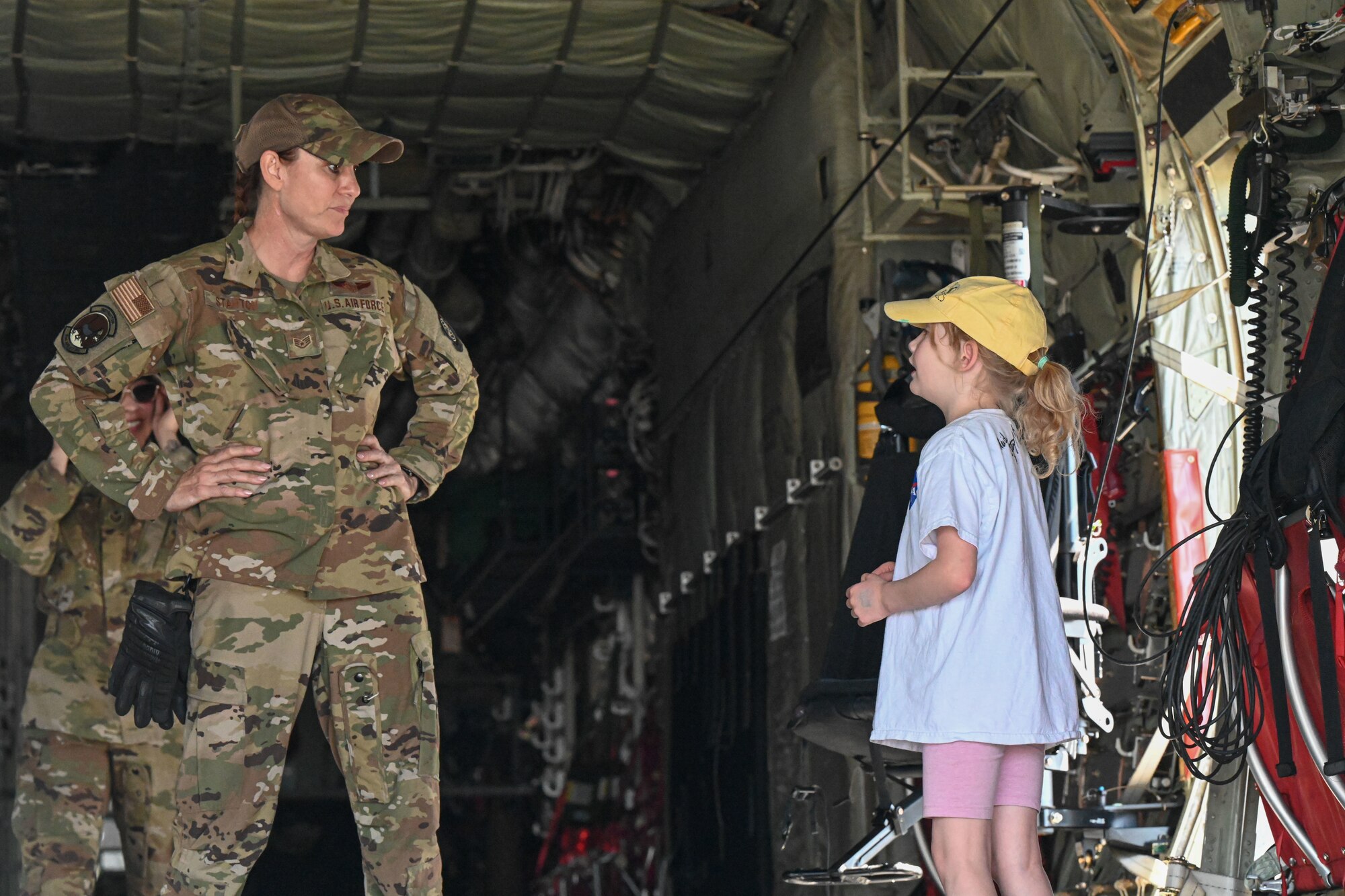 An airman speaks to a little girl in the back of a C-130J Super Hercules