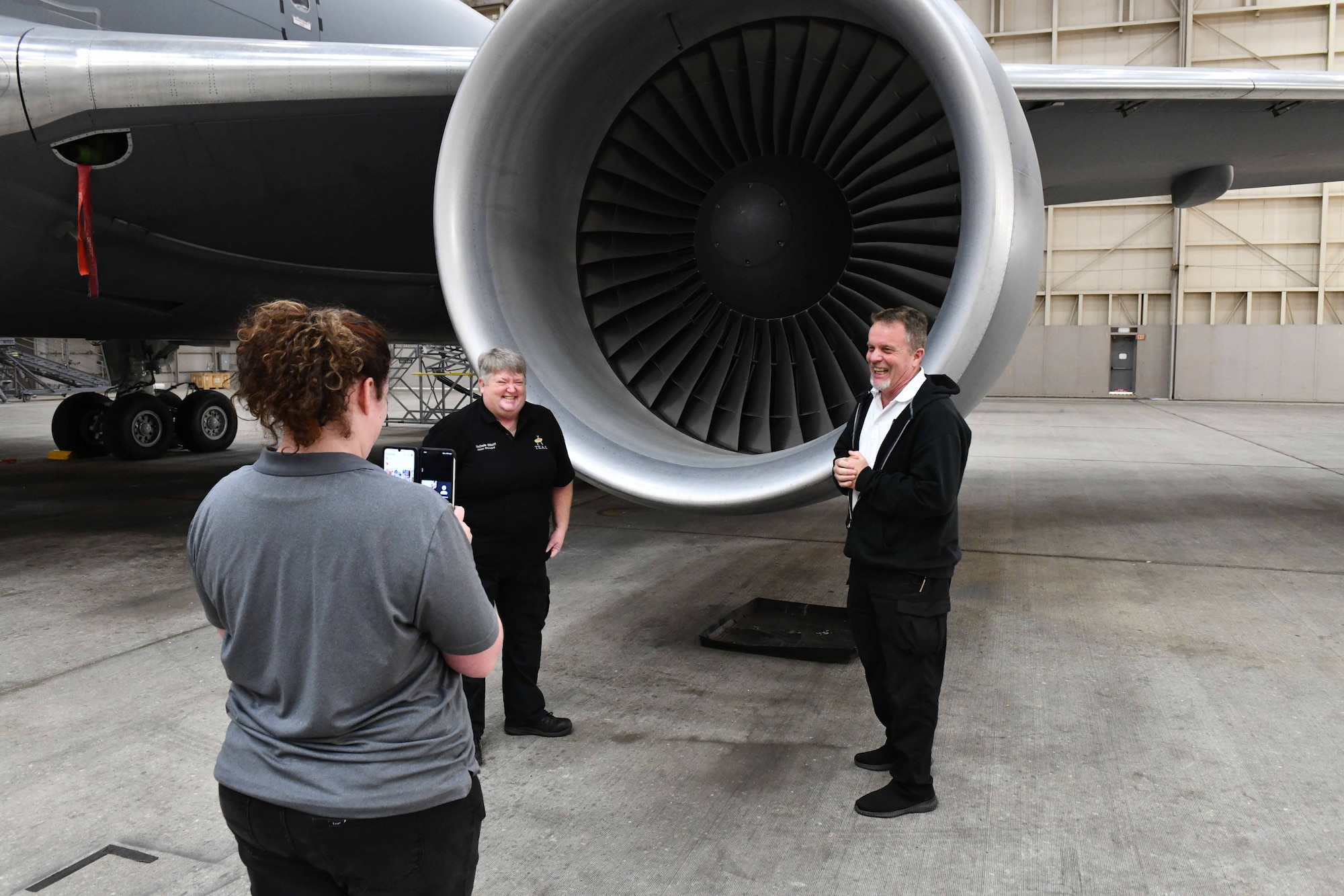 Kaitlyn Knott, 97th Maintenance Group, maintenance operations computer assistant, records a livestream of Michele Elliott, 97th Maintenance Squadron avionics technician, and Donald Obreiter, 97th Maintenance Squadron director, as they showcase a KC-46 Pegasus engine to a class of students from Hill Field Elementary School in Clearfield, Utah, via livestream at Altus Air Force Base, Oklahoma, May 1, 2023. The KC-46 has two engines that average about 16,000 flying hours before maintenance is required. (U.S. Air Force photo by Airman 1st Class Miyah Gray)